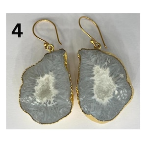 May include: A pair of gold-toned earrings featuring a grey agate stone with a white crystal centre. The earrings have a simple hook closure.