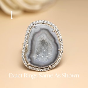 Puede incluir: Un anillo de plata con una gran piedra de ágata gris y blanca de forma ovalada. La piedra está rodeada por un halo de pequeños cristales transparentes. El anillo está sobre un fondo neutro. El texto de la imagen dice "Exact Rings Same As Shown."
