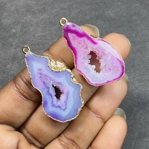 May include: Two gemstone pendants with gold-colored edges. One is a vibrant pink and white, the other a soft purple and white. Both have a central cavity and a loop for hanging. These pendants are ideal for jewelry making.