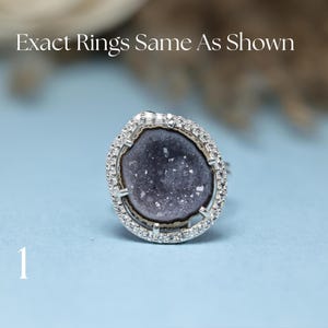 Könnte beinhalten: Ein silberner Ring mit einem dunkelvioletten, geodenartigen Mittelstein, umgeben von einem Kranz aus kleinen, klaren Steinen. Der Ring ist vor einem hellblauen Hintergrund platziert. Der Text oben lautet "Exact Rings Same As Shown" und die Zahl "1" unten.