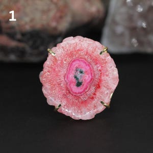 Op de afbeelding: Een roze en witte kristallen ring met een gouden zetting. De kristal heeft een uniek, draaiend patroon.