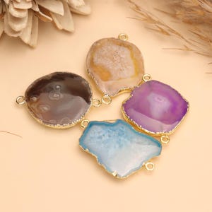 May include: Four irregular agate stone connectors with gold-toned metal edges. Each stone features a unique color, including brown, light yellow, purple, and light blue. Each connector has two small gold metal loops on opposite sides for attachment.