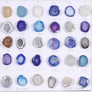 Puede incluir: Una colección de treinta piedras de ágata pulidas en varios colores, incluyendo azul, morado, blanco y marrón. Cada piedra tiene una forma y tamaño únicos, con una estructura cristalina visible. El tamaño es de 24 mm.