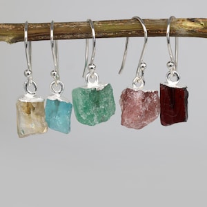 Puede incluir: Cinco pares de pendientes colgantes de plata con gotas de piedras preciosas de diferentes colores. Las piedras preciosas son de color amarillo claro, azul claro, verde, rosa y rojo.