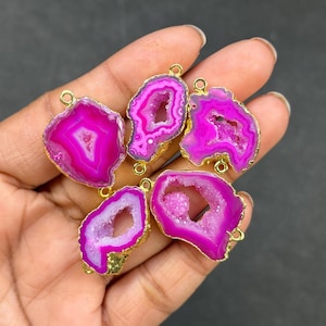May include: Five vibrant pink agate pendants with gold-colored edges and small loops for jewelry making. The pendants have a geode-like appearance, with crystal formations visible inside the pink stone.