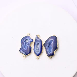 May include: Three blue and white agate gemstone pendants with gold-colored metal edges and loops. The pendants have a natural, irregular shape and a polished finish. The gemstones are set against a white background.