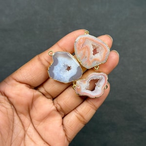 Peut inclure: Trois tranches d'agate irrégulières avec des centres cristallins, chacune encadrée par un fin bord en métal doré. Les pierres présentent des teintes translucides blanches, rose pâle et pêche avec des bandes naturelles. Chaque pièce inclut des anneaux dorés.