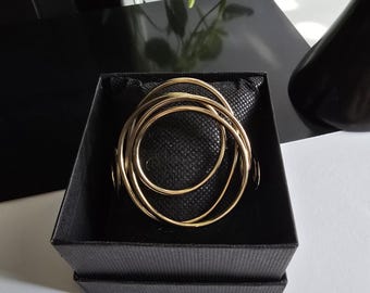Bracciale rigido a polsino, dorato, con forma a più cerchi, aperto da un lato. Comodo e leggero, elegante e stravagante. Bracciale Cuff.