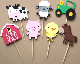 May include: A selection of farm animal and barnyard-themed cupcake toppers. The toppers include a cow, sheep, tractor, pig, chick, horse, and a red barn. Each topper is made of colourful paper and attached to a wooden stick.