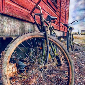 May include: Two vintage bicycles leaning against a red wooden building. The front bicycle has a large, rusty wheel with spokes. The rear bicycle has a smaller wheel and is partially obscured by the front bicycle.