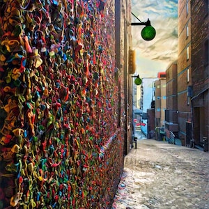 May include: A narrow alleyway with a brick wall covered in colorful chewing gum. The wall is a popular tourist attraction known as the Gum Wall. The alleyway is lined with brick buildings and streetlights.