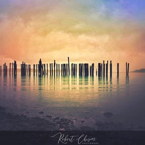 May include: A silhouette of wooden posts in a body of water at sunset. The sky is a gradient of pink, orange, and yellow. The water is calm and reflects the sky.