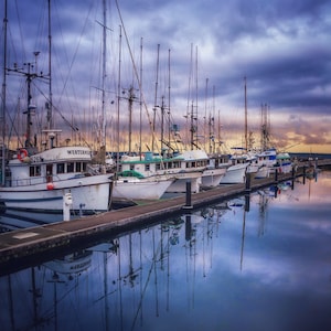 May include: A row of white fishing boats docked at a pier with a cloudy sky and calm water reflecting the boats. The boats have names like "Westerner" and "5268" on their sides.
