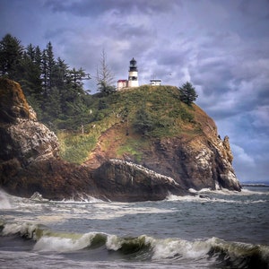 May include: A white lighthouse with a black roof sits on a rocky cliff overlooking a stormy ocean. The lighthouse is surrounded by green grass and trees. The sky is cloudy and gray.