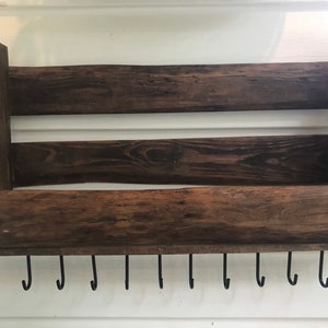 May include: Rustic wooden wall shelf with a dark brown stain and a bottom shelf with 10 black metal hooks.