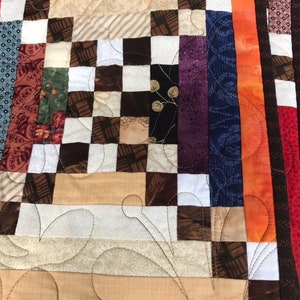 May include: A patchwork quilt with a variety of fabrics in brown, white, red, orange, blue, and purple. The quilt is made up of squares and rectangles, and the edges are finished with a border of solid fabric.