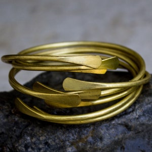 May include: A set of five gold-toned metal bangles with a unique, slightly curved design. The bangles are stacked on top of each other, creating a layered look.