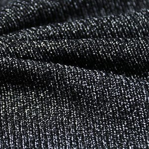 以下が含まれることがあります： 黒色のニット生地のクローズアップ。繊細で光沢のある銀色の糸が織り込まれています。ニットはリブ編みのパターンを作り、質感がはっきりと見て取れます。生地はわずかにドレープされており、折り目と影が見えます。