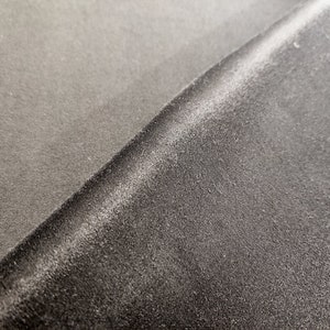 May include: Close-up of two different types of fabric. One is a smooth, dark grey fabric, and the other is a textured, dark grey fabric.