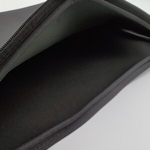 May include: Black zippered laptop sleeve with a soft, padded interior. The sleeve is open and the inside is visible.