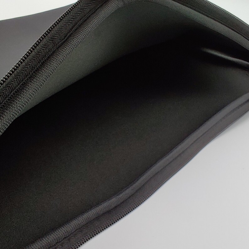 May include: Black zippered laptop sleeve with a soft, padded interior. The sleeve is open and the inside is visible.