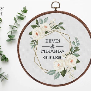 Puede incluir: Un patrón de punto de cruz floral blanco con un marco geométrico dorado. El patrón incluye los nombres "Kevin & Miranda" y la fecha "05.15.2023".