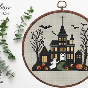 May include: Cross-stitch pattern featuring a spooky, black silhouette of a haunted house with glowing windows, bats flying overhead, and a ghost. The pattern is framed in a wooden hoop and includes the text "Modern Xstitch".