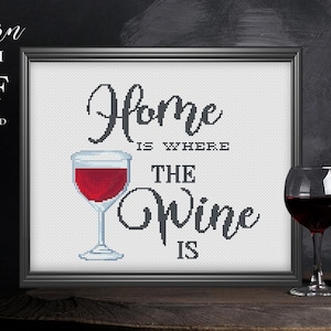 Könnte beinhalten: Gerahmtes Kreuzstich-Kunstwerk mit dem Text "Home is Where the Wine Is" und einer Weinglas-Illustration. Eine schwarze Weinflasche und ein Glas Rotwein befinden sich neben dem Kunstwerk. Sofortiger PDF-Download.