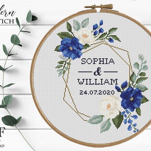 Pu&ograve; includere: Schema di punto croce con una ghirlanda floreale con fiori blu e bianchi, una cornice geometrica dorata e il testo "Sophia & William 24.07.2020".