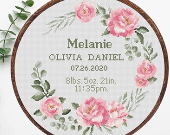 May include: A white embroidery hoop with a floral design in pink and green. The hoop includes the text "Melanie Olivia Daniel 07.26.2020 8lbs 5oz 21in. 11:35pm."