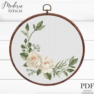May include: A cross-stitch floral design in a wooden embroidery hoop. The design features white roses and green leaves. The text "Modern XStitch" is at the top left, and "PDF Instant Download" is at the bottom right.