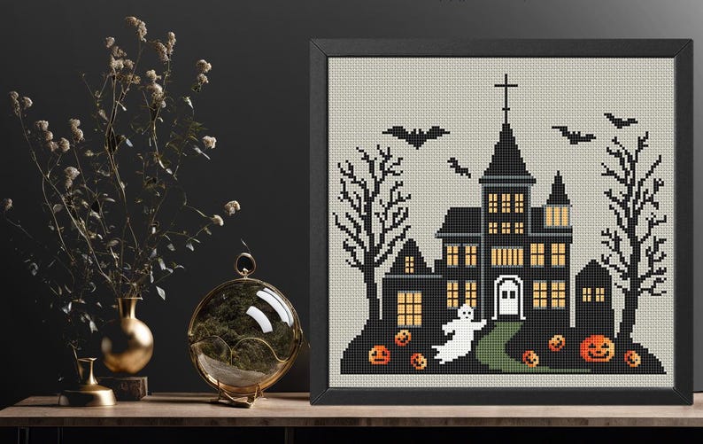May include: A black and white cross-stitch pattern of a spooky haunted house with a ghost, bats, and pumpkins. The house has lit windows and a front door. The background is a light grey.