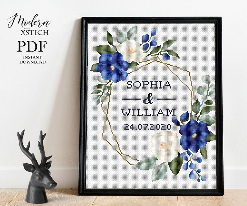 Pu&ograve; includere: Schema di punto croce con una ghirlanda di fiori blu e bianchi, una cornice geometrica dorata e il testo "Sophia & William 24.07.2020".