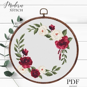 May include: A cross-stitch floral design in a wooden embroidery hoop. The design features a wreath of red and white roses with green leaves. The text "Modern XSTICH" and "PDF INSTANT DOWNLOAD" are visible.
