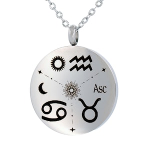 May include: A silver-toned circular pendant necklace featuring black engraved astrological symbols including a sun, Aquarius waves, a crescent moon, Cancer, and Taurus signs, with a central starburst design and the text Asc printed on the surface.