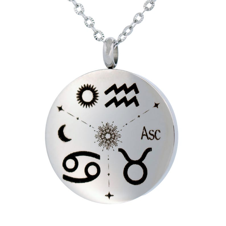 May include: A silver-toned circular pendant necklace featuring black engraved astrological symbols including a sun, Aquarius waves, a crescent moon, Cancer, and Taurus signs, with a central starburst design and the text Asc printed on the surface.