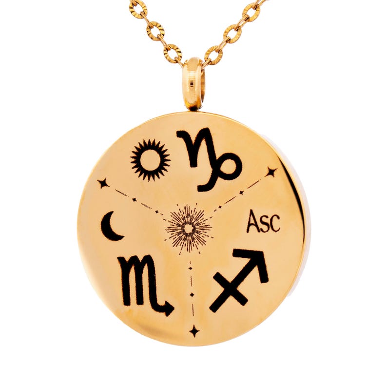 May include: A gold-toned circular pendant necklace featuring black engraved astrological symbols including a sun, moon, Capricorn, Scorpio, and Sagittarius signs, along with the text Asc, all arranged around a central starburst design.