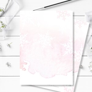 May include: A blank white card with a pink watercolor background and white snowflake designs. The card is perfect for writing a message or creating a custom design.
