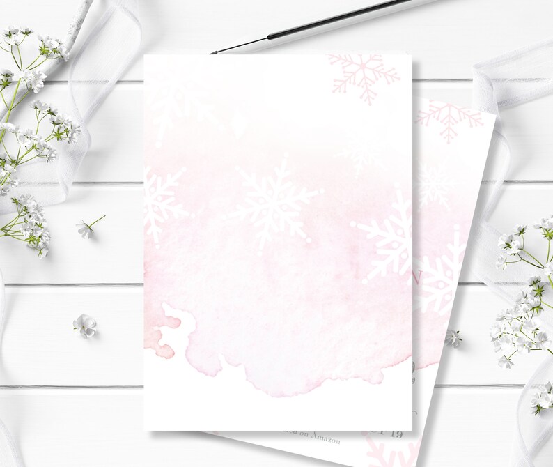 May include: A blank white card with a pink watercolor background and white snowflake designs. The card is perfect for writing a message or creating a custom design.