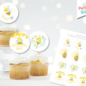 Puede incluir: Cupcakes cubiertos con adornos redondos con ilustraciones de abejas en acuarela. Algunos adornos dicen "Mummy to Bee" y "Welcome Bebel". Se ve una hoja de adornos adicionales, con el texto "Parties by the Bundle".