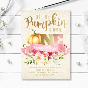 May include: A beige invitation card with gold lettering that reads "Our Little Pumpkin is Turning One." It features a watercolor pumpkin, pink floral accents, and a pink banner with a name. The card is for a first birthday celebration.
