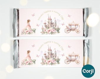 Könnte beinhalten: Zwei rosa Schokoriegelverpackungen mit silbernen Folienenden. Jede Verpackung zeigt eine Prinzessin, ein Schloss, eine Kutsche und Schmetterlinge. Der Text lautet "Princess Sophia is turning ONE". Die Website-Adresse ist oben sichtbar.