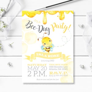 May include: A yellow and white bee-themed birthday party invitation with a cartoon bee illustration. The invitation reads "It's a Bee-Day Party!" and includes the name "Isla Rose" and the text "is turning ONE!"  The invitation also includes the date, time, and location of the party.