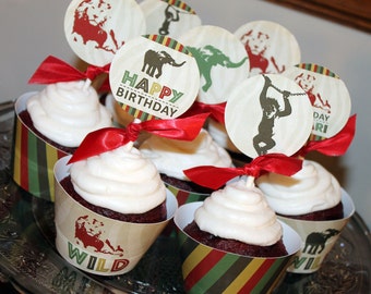 May include: Red velvet cupcakes decorated with white frosting and topped with animal-themed cupcake toppers. The toppers feature a lion, an elephant, a monkey, and the text "Happy Birthday" and "Wild".