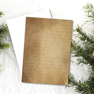 May include: A blank card with a brown paper texture and faint writing. The card is on a white fluffy surface with green pine branches and gold ornaments.
