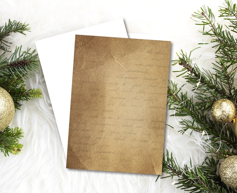 May include: A blank card with a brown paper texture and faint writing. The card is on a white fluffy surface with green pine branches and gold ornaments.