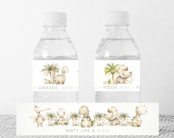May include: Two clear plastic water bottles with labels featuring a dinosaur and palm tree design. The labels read "Jurassic Juice" and "Fossil Fuel". A banner below reads "Party Like A Dino!" with a website address.