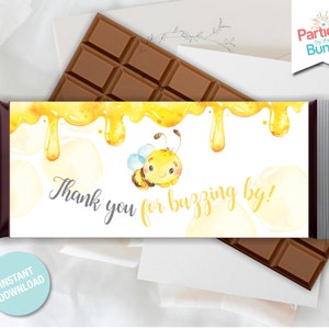 May include: A white chocolate bar wrapper with a yellow and white watercolor design of honey dripping and a cartoon bee. The wrapper says "Thank you for buzzing by!"