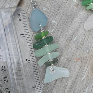 Puede incluir: Un collar de vidrio de mar con dise&ntilde;o de pez. El pez est&aacute; hecho de diferentes tonos de vidrio de mar verde y azul, ensartados con alambre plateado. El collar mide aproximadamente 7,6 cm de largo.