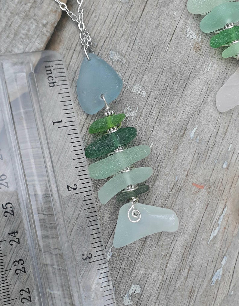 Puede incluir: Un collar de vidrio de mar con dise&ntilde;o de pez. El pez est&aacute; hecho de diferentes tonos de vidrio de mar verde y azul, ensartados con alambre plateado. El collar mide aproximadamente 7,6 cm de largo.